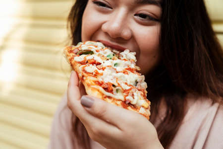 Cropped image of homemade pizza is eaten by the fat woman at the yellow shutter door.