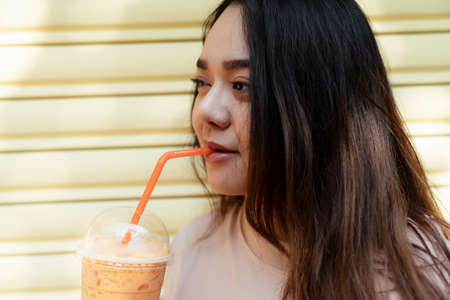 Long hair fat woman drink Thai milk tea with orange straw.の写真素材