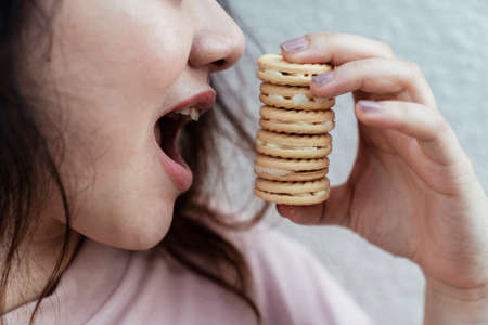 Close up shot of long hair fat woman while she try to eat six biscuit in the same time in front of white wall.の写真素材