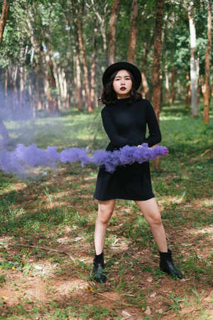 A black dress witch playing purple smoke torches in the forest.