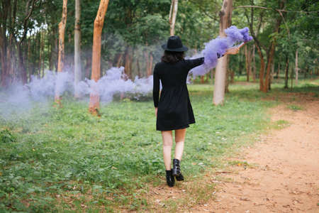 A black dress witch playing purple smoke torches in the forest.