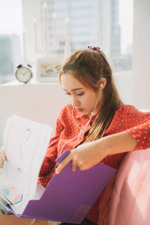 Work from home concept - Beautiful young woman in red pajamas shirt sitting on a couch working on...