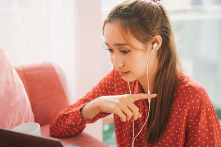 Work from home concept - Beautiful young woman in red pajamas shirt using earphones talking with...