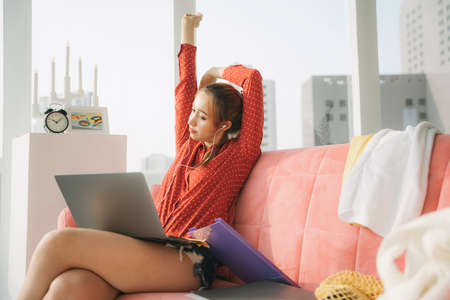 Work from home concept - Beautiful young woman in red pajamas shirt stretching hands after working...