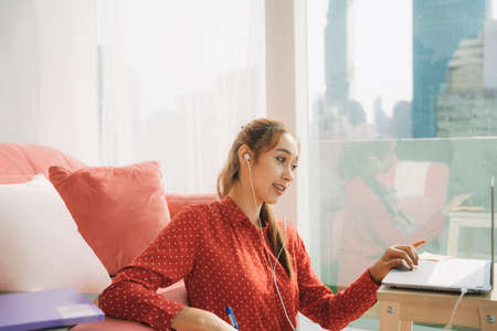 Work from home concept - Beautiful young woman in red pajamas shirt working on laptop at home because of Covid-19 epidemic. Quarantine.の写真素材