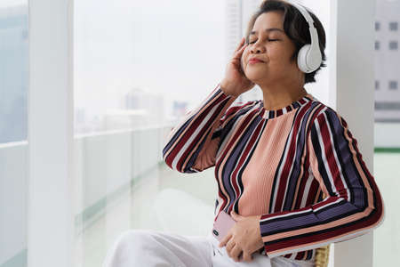 Portrait of old elderly senior woman enjoy listen to music with headphone and smartphone.