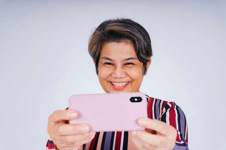 Cheerful happy old elderly senior woman taking selfie or vlogging with smartphone.