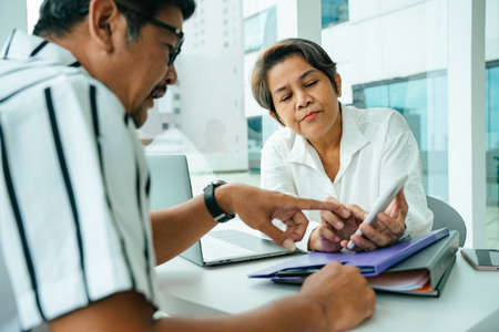 Adult asian businessman working with partner together on smartphone in office room.の写真素材