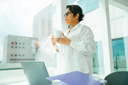 Old elderly senior woman holding coffee cup at office room.