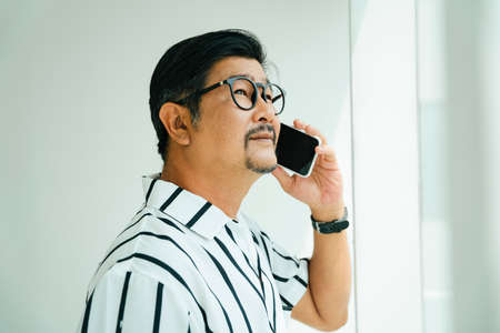 Old elderly senior man in casual white collar shirt talking on the phone.の写真素材