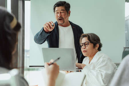 Old elderly senior ceo and secretary making presentation in meeting room. He asking team for opinion.の写真素材