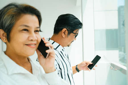 Side view of elderly senior couple using smartphone at window.