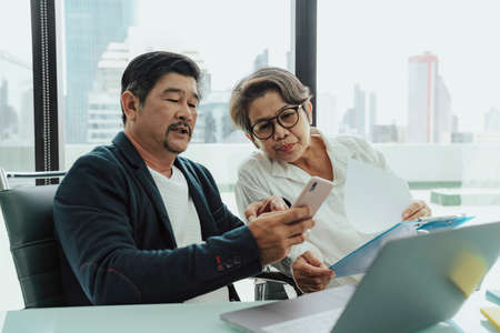 Old elderly senior business people working on laptop and smartphone in meeting room.の写真素材