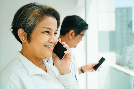 Side view of elderly senior couple using smartphone at window.の写真素材