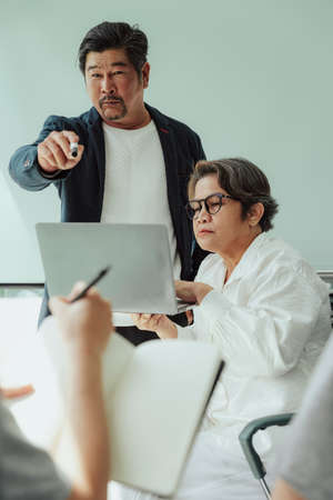 Old elderly senior ceo and secretary making presentation in meeting room. He asking team for opinion.の写真素材