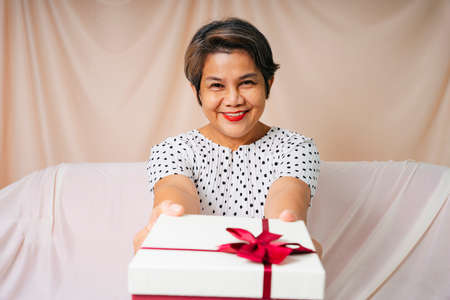 Portrait of cool old elderly senior woman in white polka dot dress with birthday gift box.の写真素材