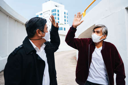 Fashion portrait of two old elderly senior people wearing mask doing high five.の写真素材