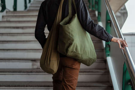 A man in black shirt and brown pants walk up the stair with green canvas bag.の写真素材