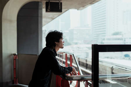 Black hair guy rest his arms on the barricade of skytrain station and look around.の写真素材