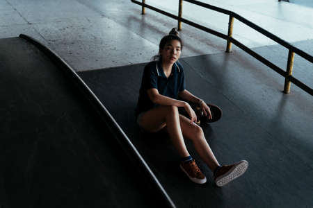 Woman in dark blue polo shirt sitting on the slope with her longboard while take a break.の写真素材