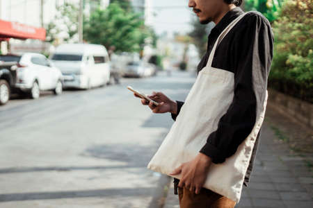 Cropped image of smartphone in a man's hand with white canvas bag on his shoulder.の写真素材