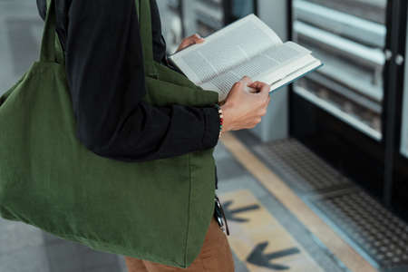 Cropped image of opened book in a man's hands while he standing at skytrain station waiting for the train.の写真素材