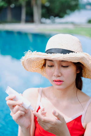 Beautiful asian woman traveler apply cream sunblock lotion at swimming pool.の写真素材