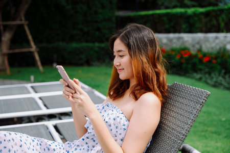 Beautiful asian woman using smartphone on beach chair in hotel.の写真素材