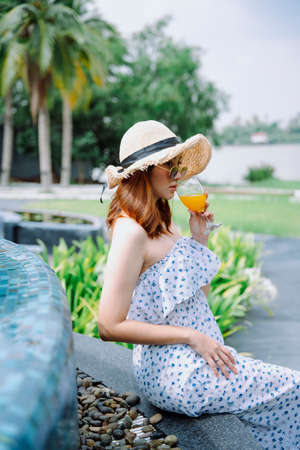 Side view - Beautiful asian woman traveler enjoy drinking orange juice at poolside.の写真素材