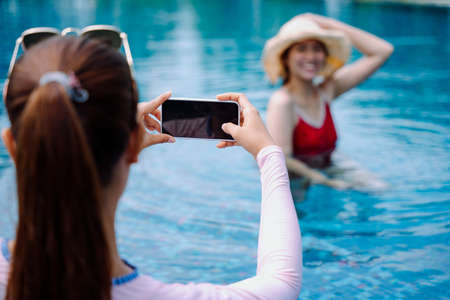 Beautiful asian women traveler enjoy taking photo in swimming pool with smartphone.の写真素材