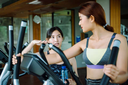 Beautiful healthy woman work out on machine with trainer at gym.の写真素材