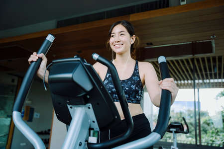 Happy beautiful healthy woman exercising on gym bike indoors.