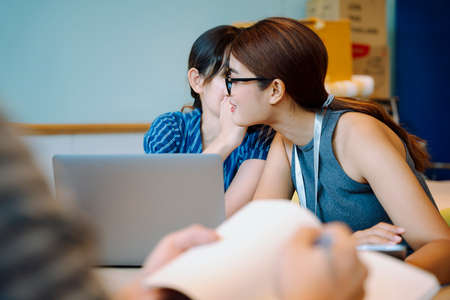 Asian business women gossip to her friend in conference room.