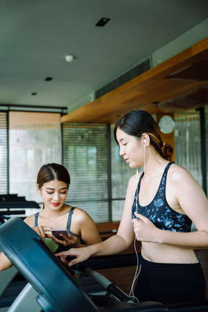 Beautiful healthy woman running on treadmill with trainer beside the machine.
