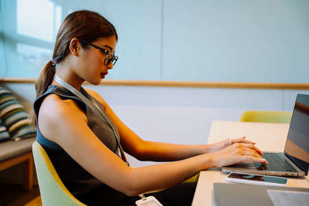 Side view - Asian business woman wear eyeglasses typing on laptop computer.
