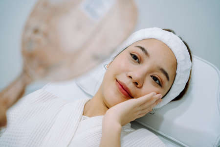 Asian woman looking at mirror after finish spa treatment in beauty clinic.の写真素材