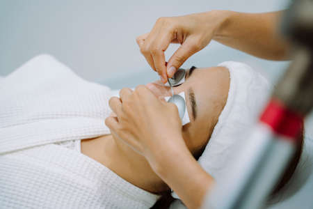 Asian woman getting facial spa treatment with protective goggles during cosmetic procedure.の写真素材