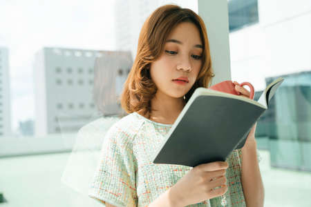 Portrait of beautiful young asian woman read a book and drink a cup of coffee.
