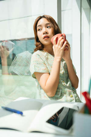 Asian student woman take a break drink a cup of coffee in a room.