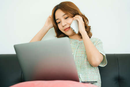 Asian woman talking on smartphone and working with laptop at home.の写真素材