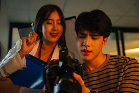 Asian photographer with camera talking to assistant in studio indoors.
