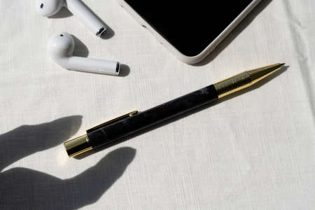 Top view - business office desk with golden pen, earphone, and smartphone over white background.
