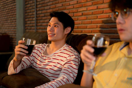 Couple of asian LGBTQ+ men enjoy drinking wine and watching TV together at home.の写真素材