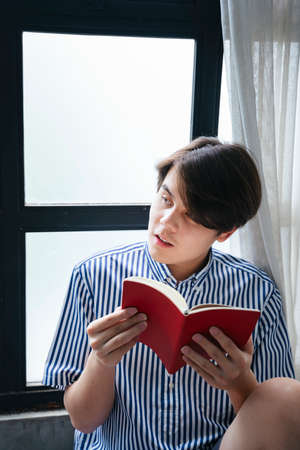 Asian young man as a student reading red book for exam.