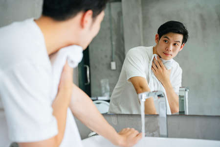 Asian young man washing and cleaning face with towel in bathroom.の写真素材