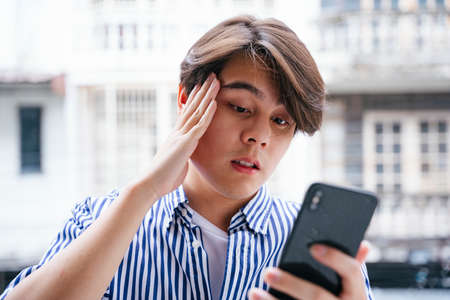 Asian young man having problem paying bill on smartphone.