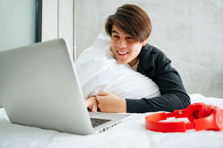 Asian young man watching movie in bedroom in the morning.の写真素材
