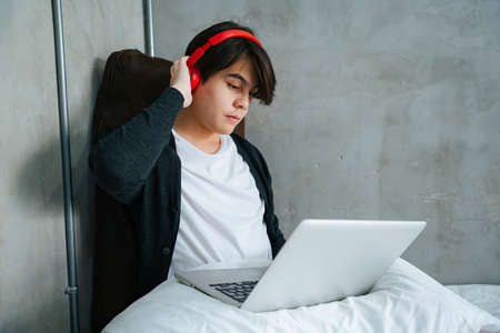 Asian young man listen to music with headphone and looking at laptop computer.の写真素材