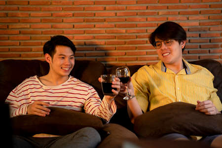 Couple of asian LGBTQ+ men celebrate anniversary with wine at home.