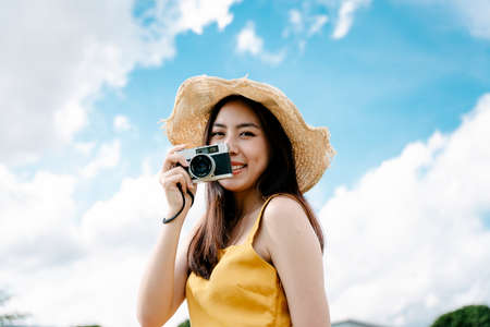 Beautiful asian traveler woman taking photo with vintage film camera on bright sky background.